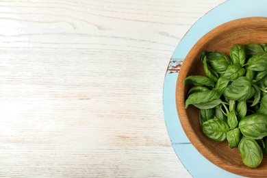 Fresh green basil leaves in bowl and board on wooden background, top view with space for text