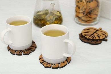 Photo of Hot beverage and stylish wooden cup coasters on white table