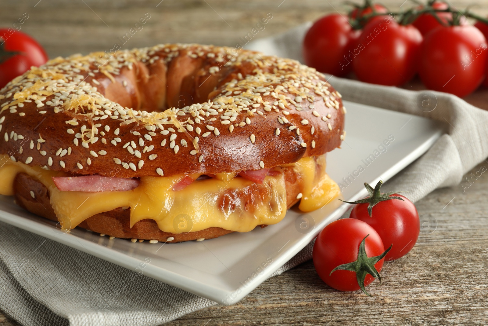 Photo of Delicious bagel with ham, cheese and tomatoes on wooden table