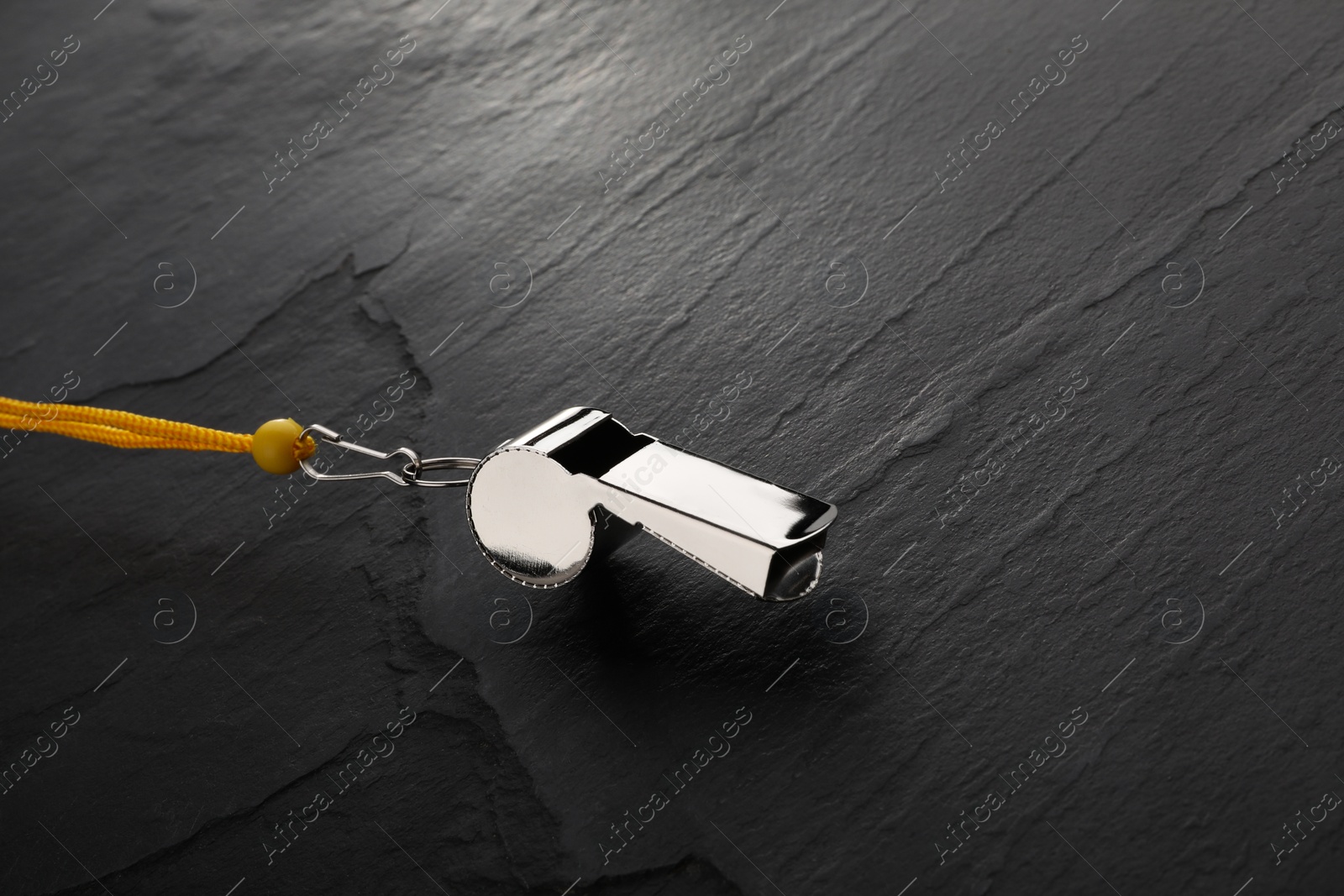 Photo of Referee equipment. Metal whistle on black textured background, closeup and space for text