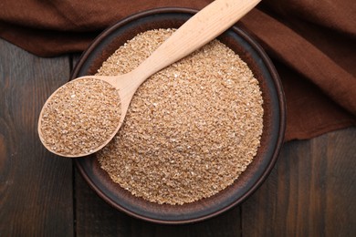 Photo of Dry wheat groats in bowl and spoon on wooden table, top view