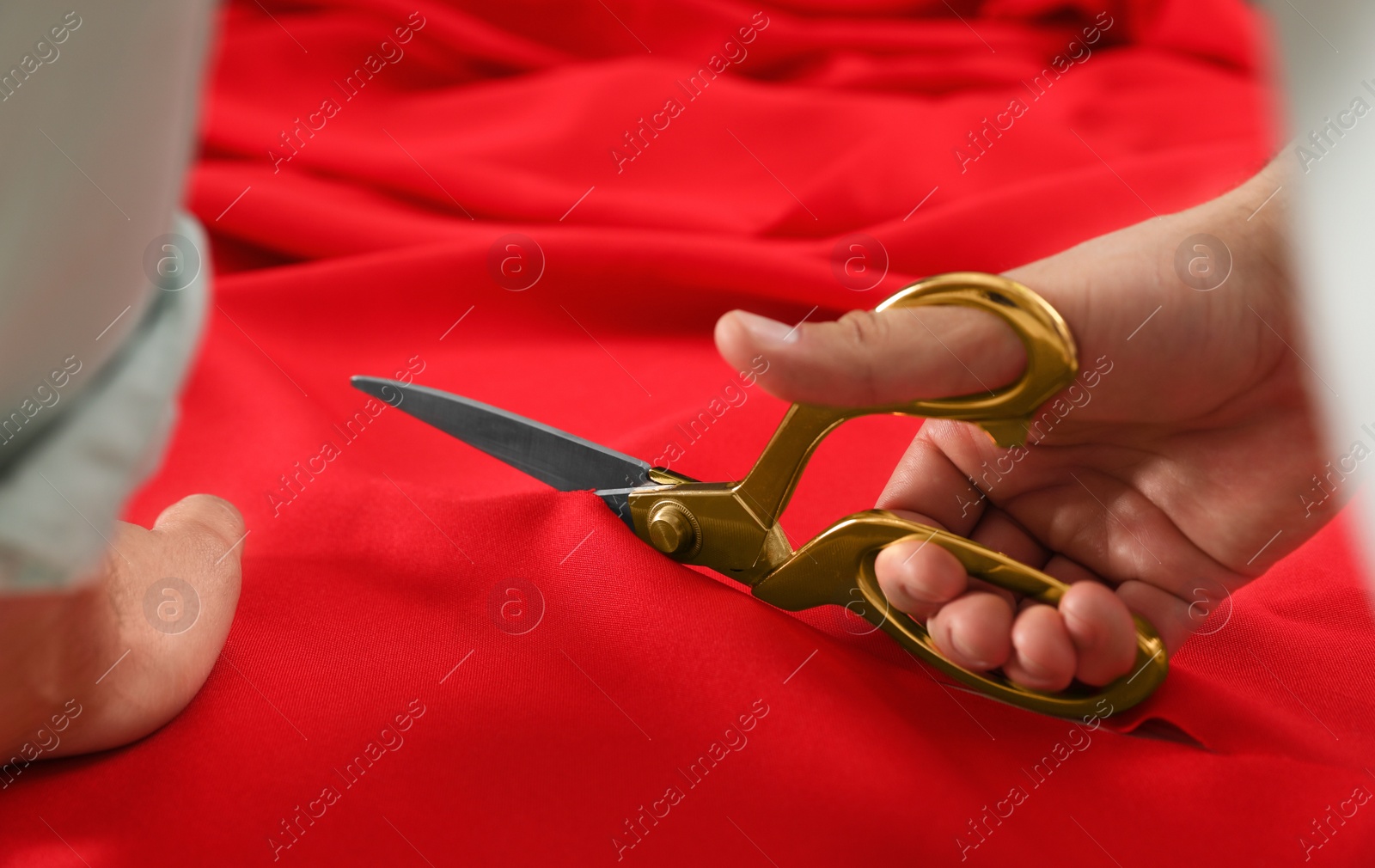 Photo of Professional tailor cutting red fabric with scissors in workshop, closeup