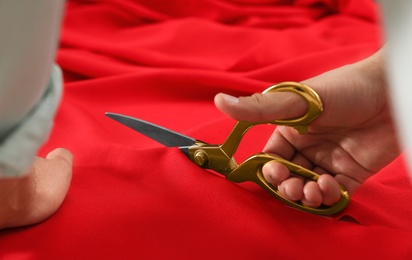 Professional tailor cutting red fabric with scissors in workshop, closeup