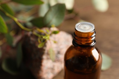 Bottle of eucalyptus essential oil, stone and leaves on wooden table, closeup. Space for text