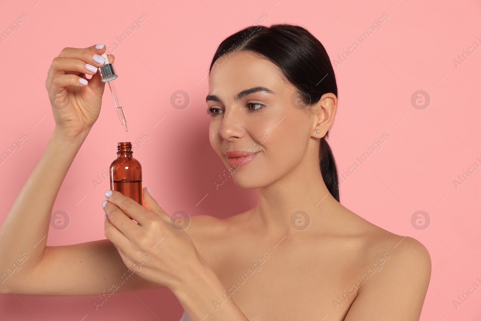 Photo of Young woman with bottle of essential oil on pink background