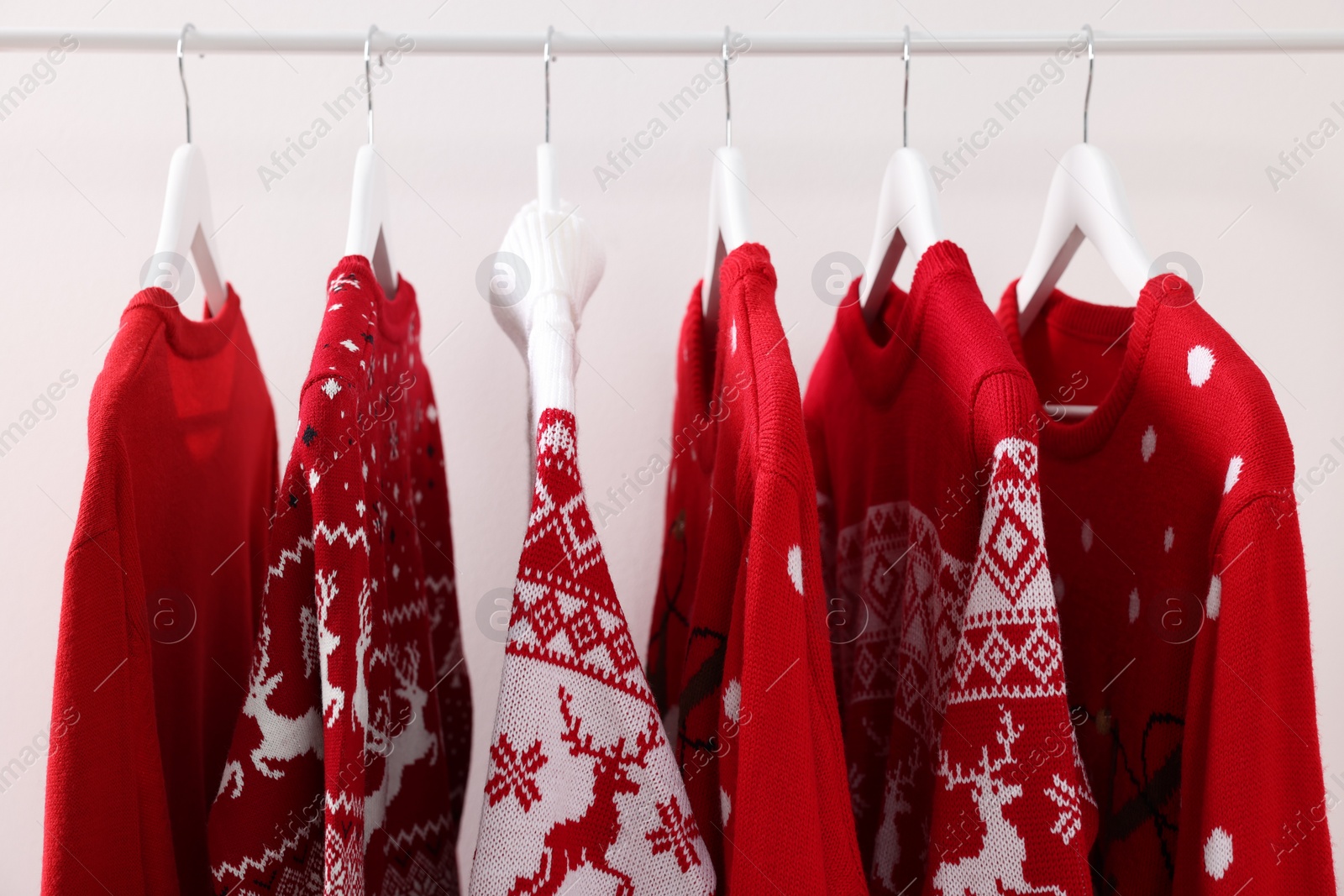 Photo of Rack with different Christmas sweaters on white background, closeup