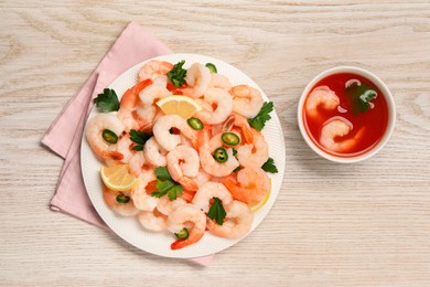 Photo of Tasty boiled shrimps with cocktail sauce, chili, parsley and lemon on light wooden table, flat lay