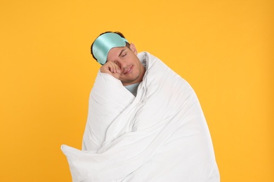Man wrapped with blanket in sleeping mask on yellow background
