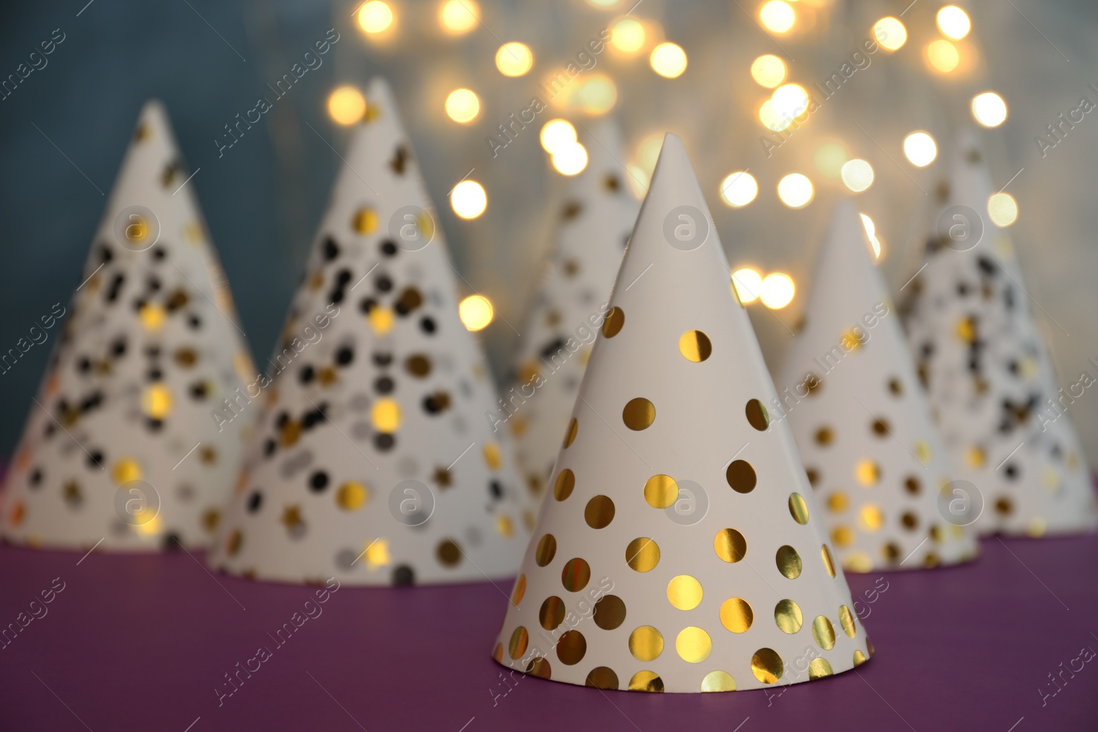 Photo of Beautiful party hats on purple table against blurred lights