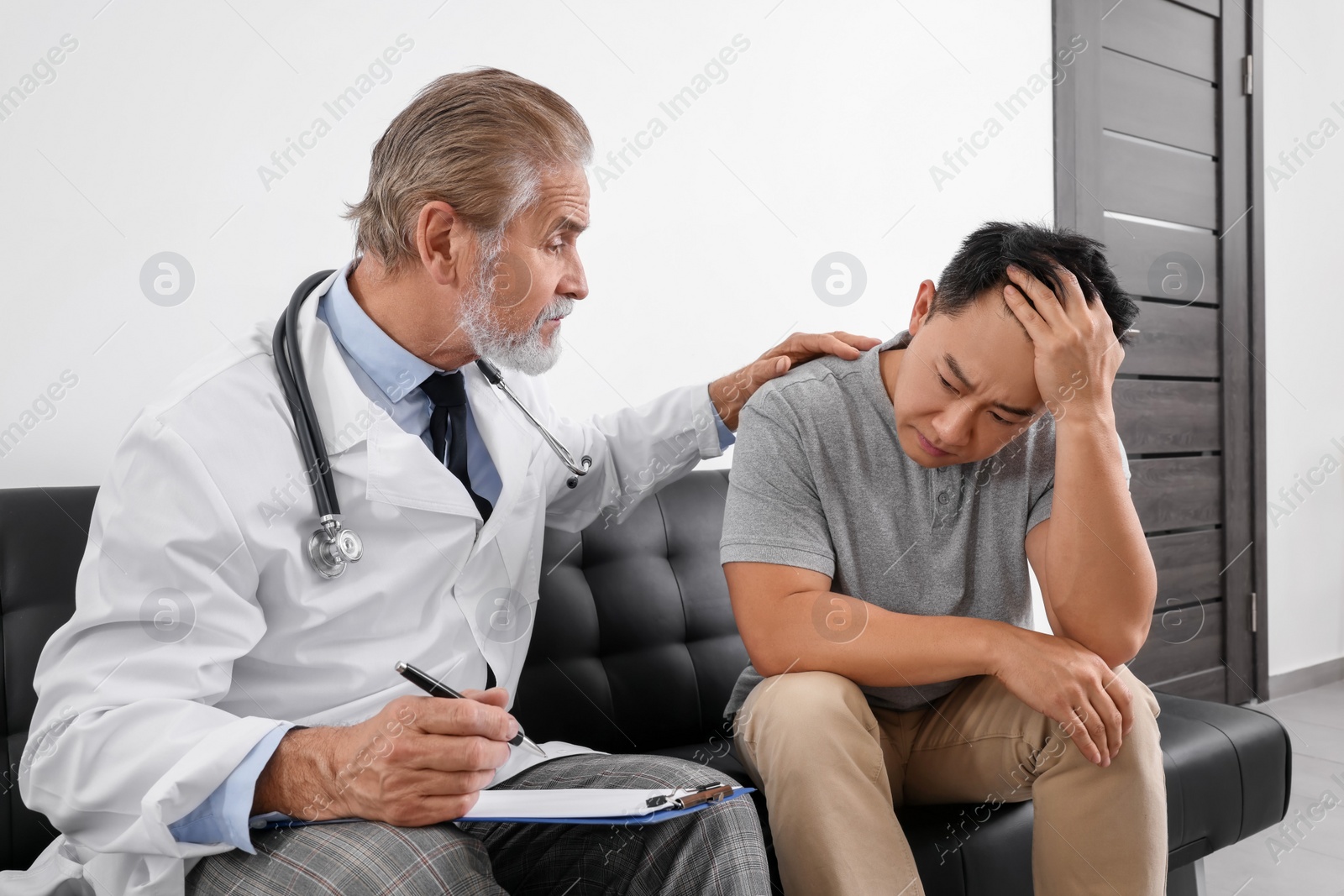 Photo of Senior doctor with clipboard consulting upset patient in clinic