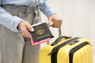 Photo of Woman with suitcase giving passport and tickets on blurred background, closeup