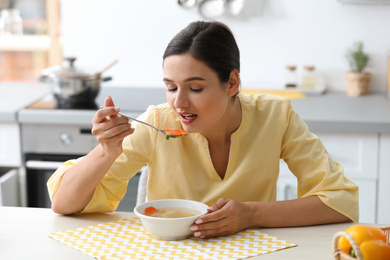 Photo of Young woman eating tasty vegetable soup at table in kitchen