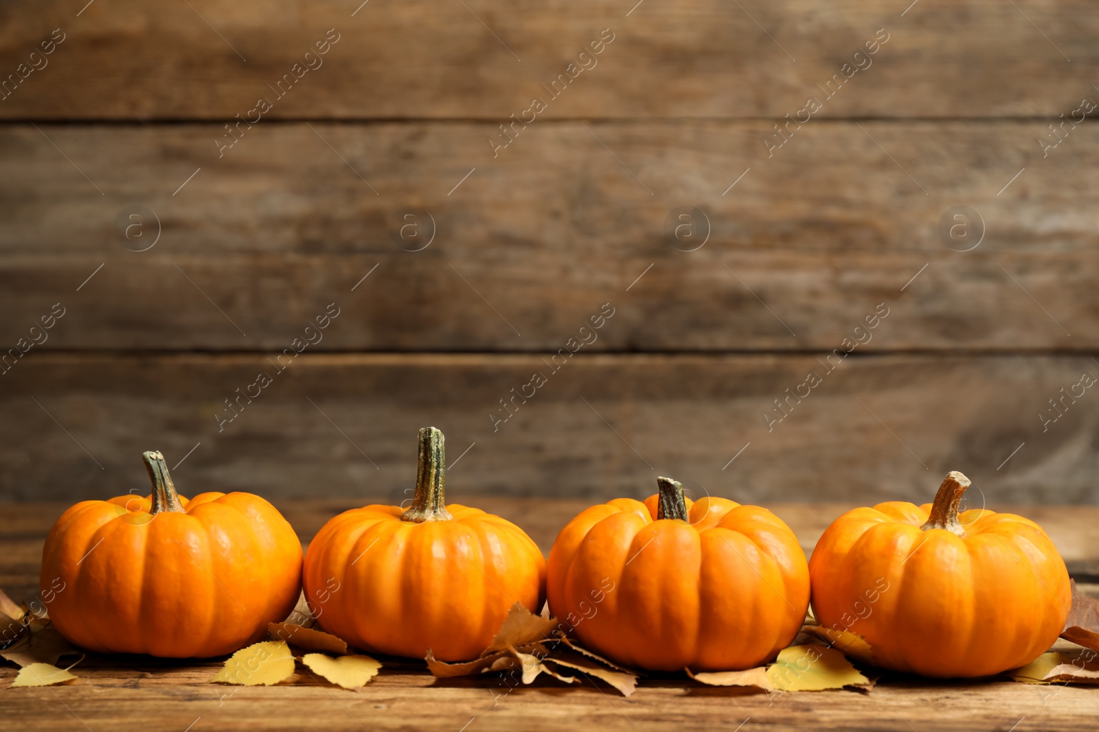 Photo of Ripe orange pumpkins and autumn leaves on wooden table. Space for text