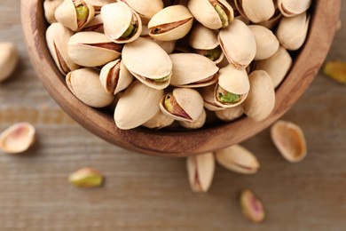 Photo of Tasty pistachios in bowl on wooden table, top view