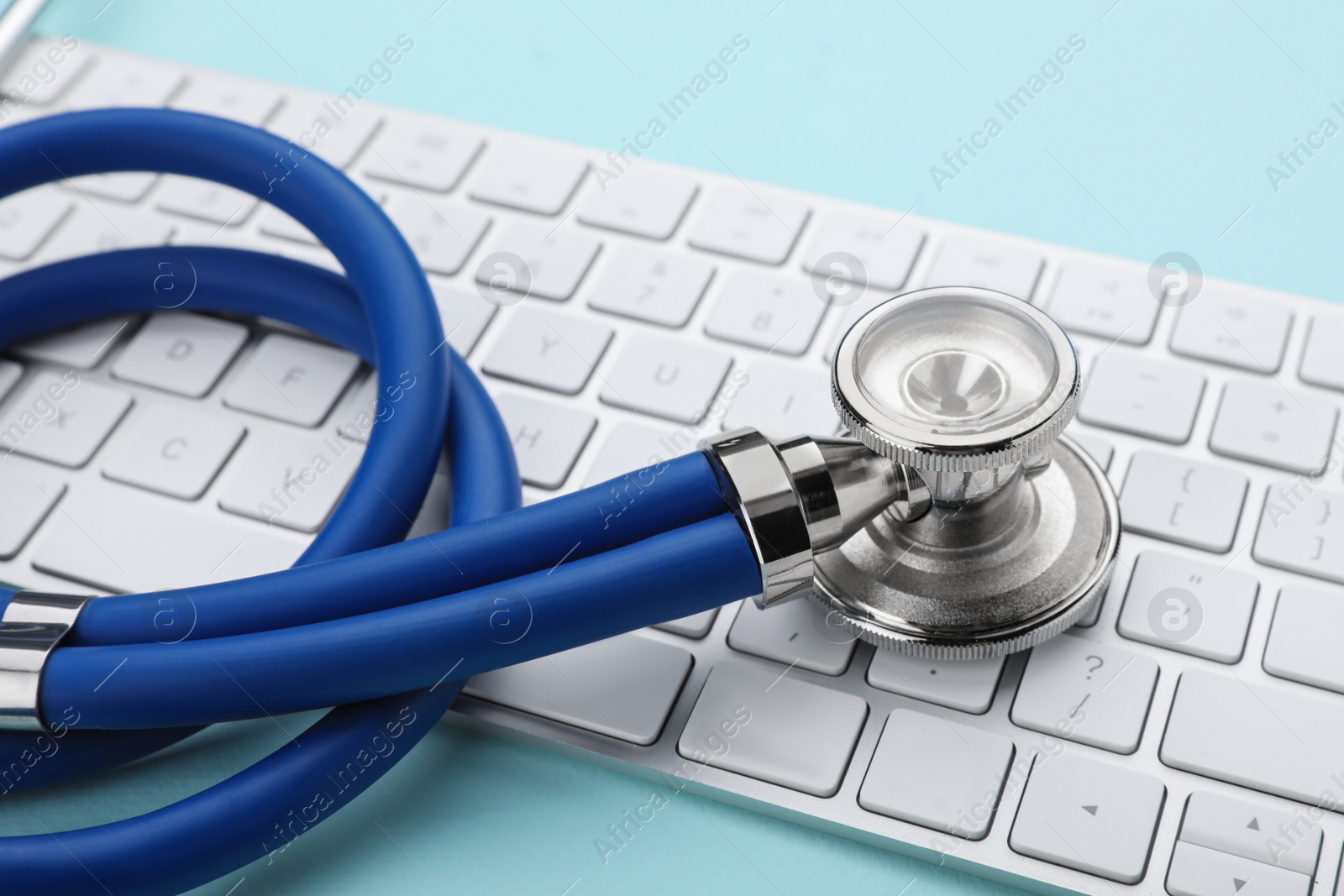 Photo of Computer keyboard with stethoscope on turquoise background, closeup