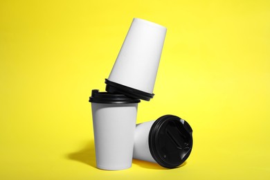 Photo of Paper cups with black lids on yellow background. Coffee to go