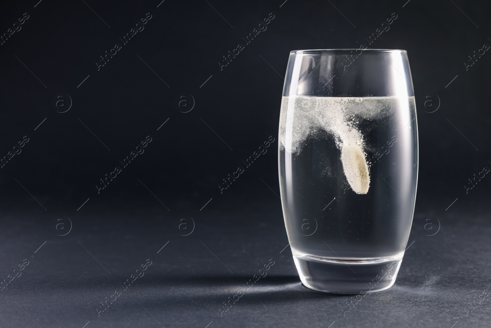 Photo of Effervescent pill dissolving in glass of water on grey table. Space for text