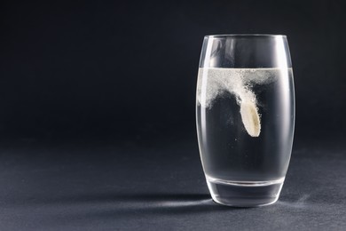 Effervescent pill dissolving in glass of water on grey table. Space for text