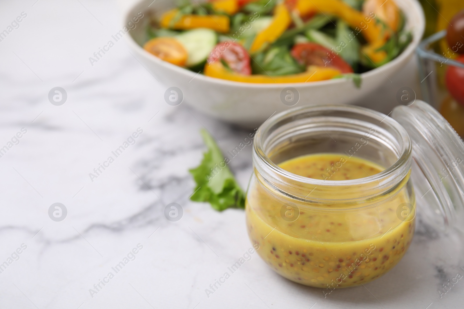 Photo of Tasty vinegar based sauce (Vinaigrette) in jar on white marble table, closeup. Space for text