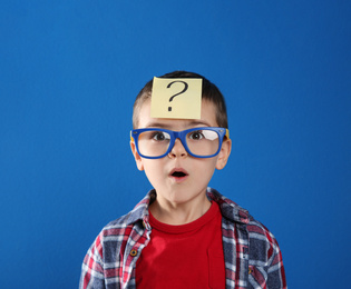 Photo of Emotional little boy with question mark on blue background