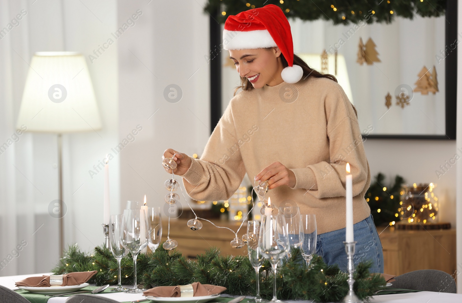 Photo of Smiling woman in Santa hat setting table for Christmas celebration at home