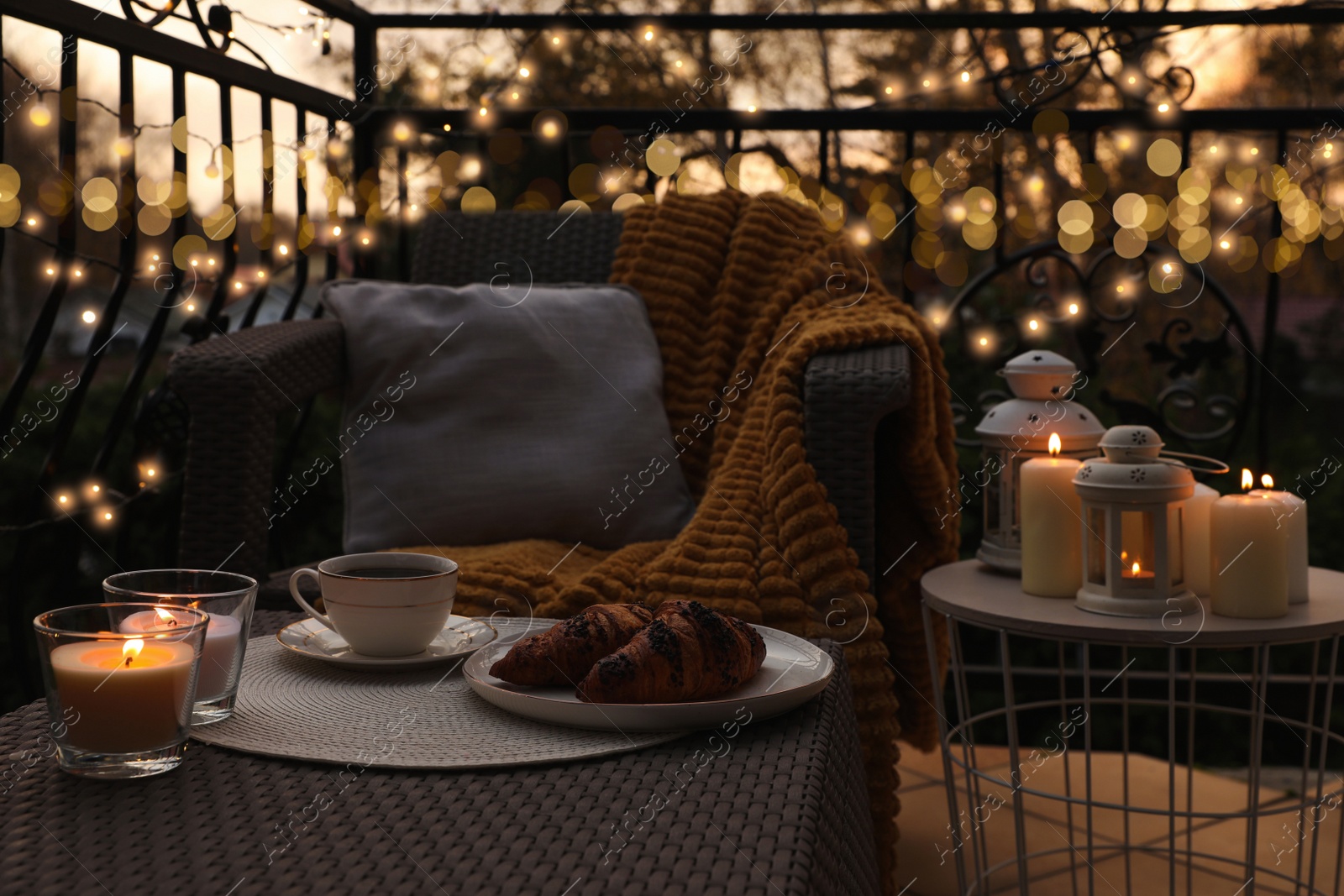 Photo of Beautiful view of garden furniture with pillow, soft blanket and burning candles at balcony