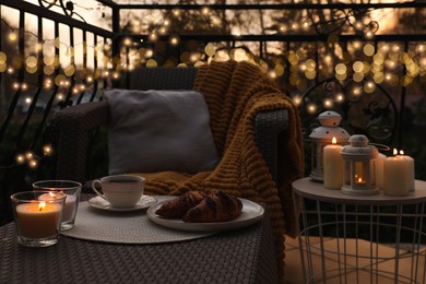 Photo of Beautiful view of garden furniture with pillow, soft blanket and burning candles at balcony