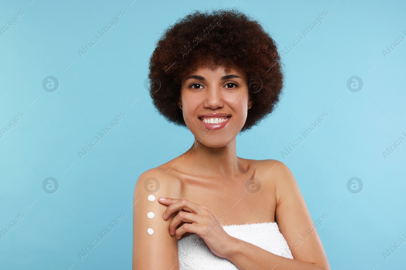 Photo of Beautiful young woman applying body cream onto arm on light blue background