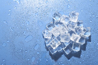 Pile of melting ice cubes and water drops on blue background, top view. Space for text