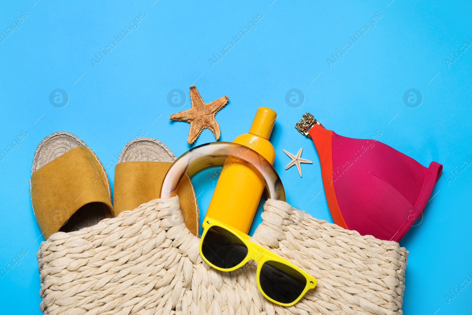 Photo of Bag with beach accessories on light blue background, flat lay