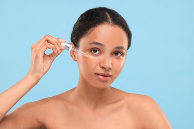 Photo of Beautiful woman applying serum onto her face on light blue background