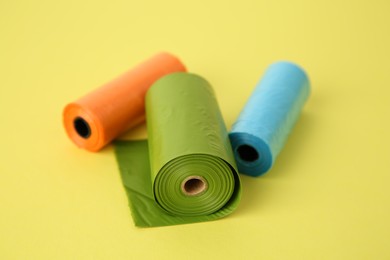 Photo of Colorful dog waste bags on yellow background, closeup