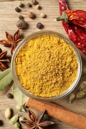 Curry powder in bowl and other spices on wooden table, flat lay