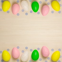 Many decorated Easter eggs and confetti on wooden table, flat lay. Space for text