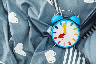 Analog alarm clock on bed, top view. Time of day