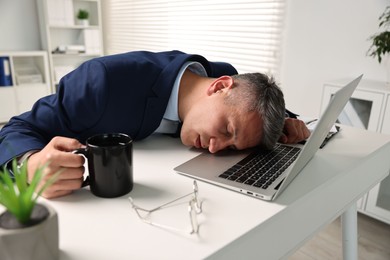 Man with cup of drink sleeping at table in office