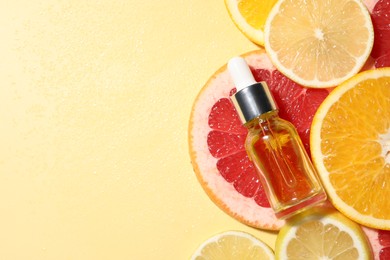 Photo of Bottle of cosmetic serum and sliced citrus fruits on yellow background, flat lay. Space for text