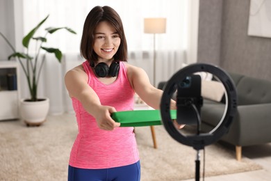 Happy sports blogger holding resistance band while streaming online fitness lesson with smartphone at home