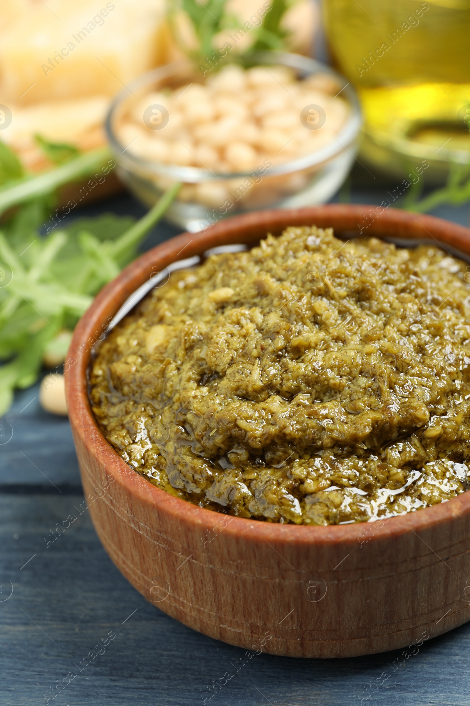 Photo of Bowl of tasty arugula pesto on blue wooden table, closeup