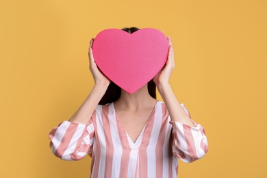 Photo of Young woman with decorative heart near face on color background