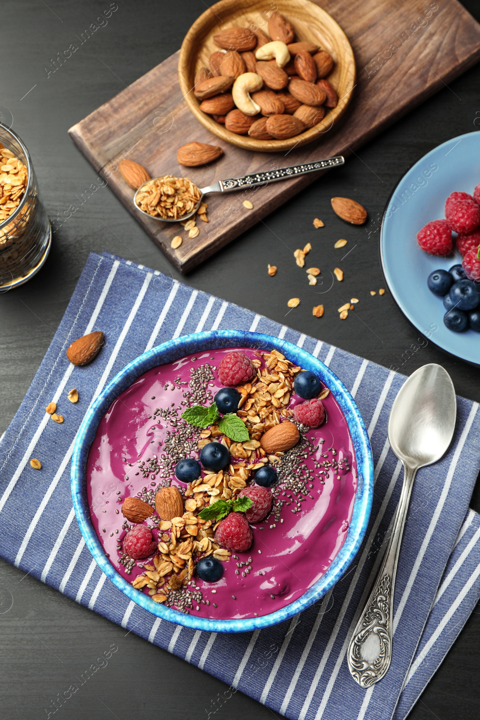 Photo of Delicious acai smoothie with granola and berries in dessert bowl served on dark wooden table, flat lay