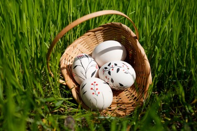 Photo of Wicker basket with decorated Easter eggs in green grass outdoors