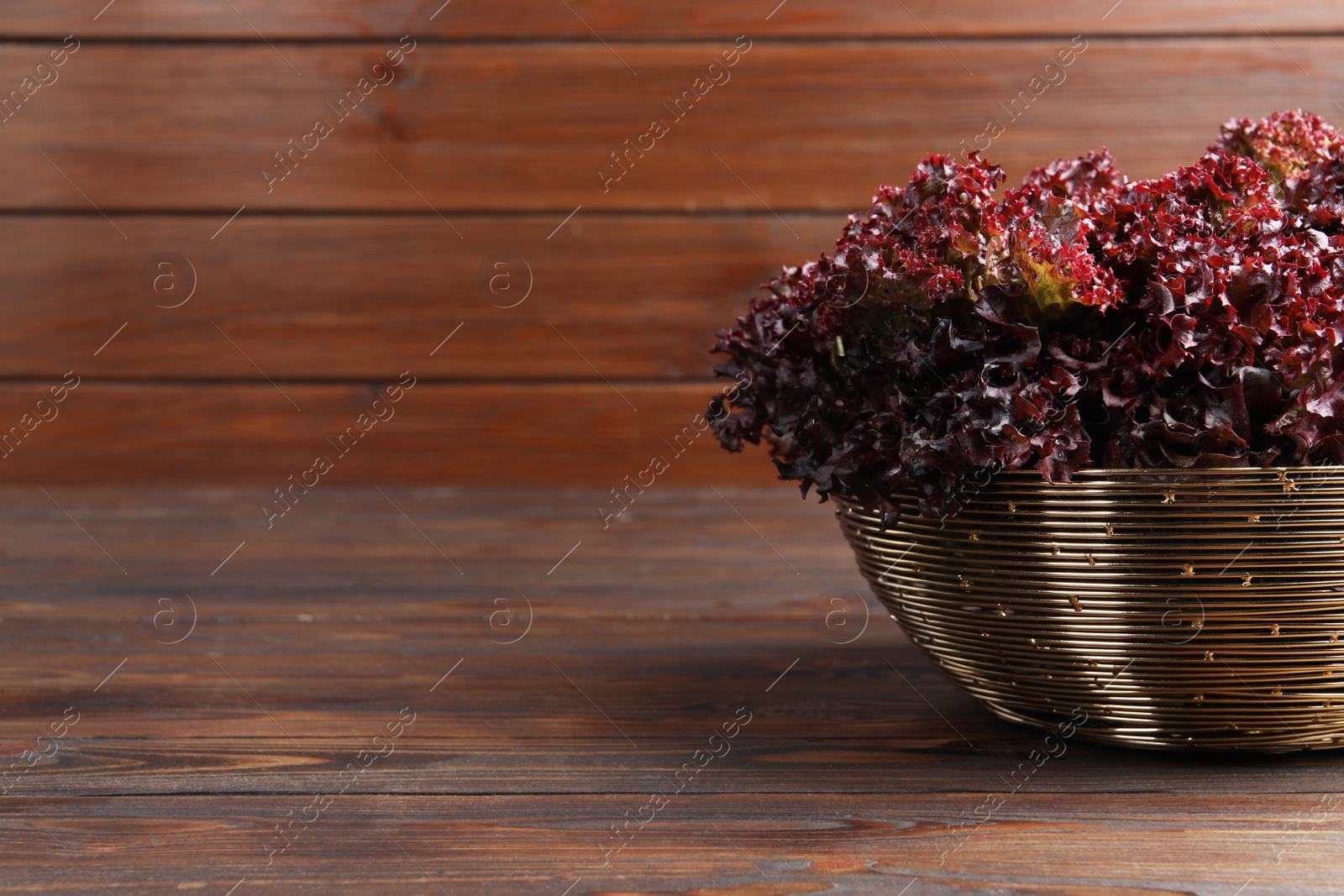 Photo of Bowl with fresh red coral lettuce on wooden table, space for text