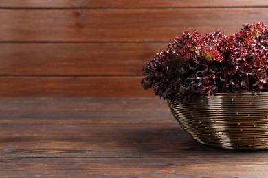Photo of Bowl with fresh red coral lettuce on wooden table, space for text