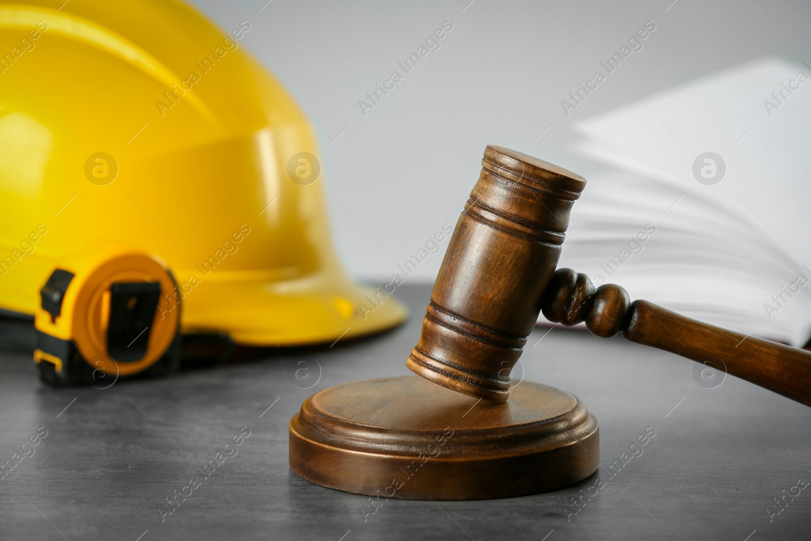 Photo of Construction and land law concepts. Judge gavel, open book, tape measure with protective helmet on grey table