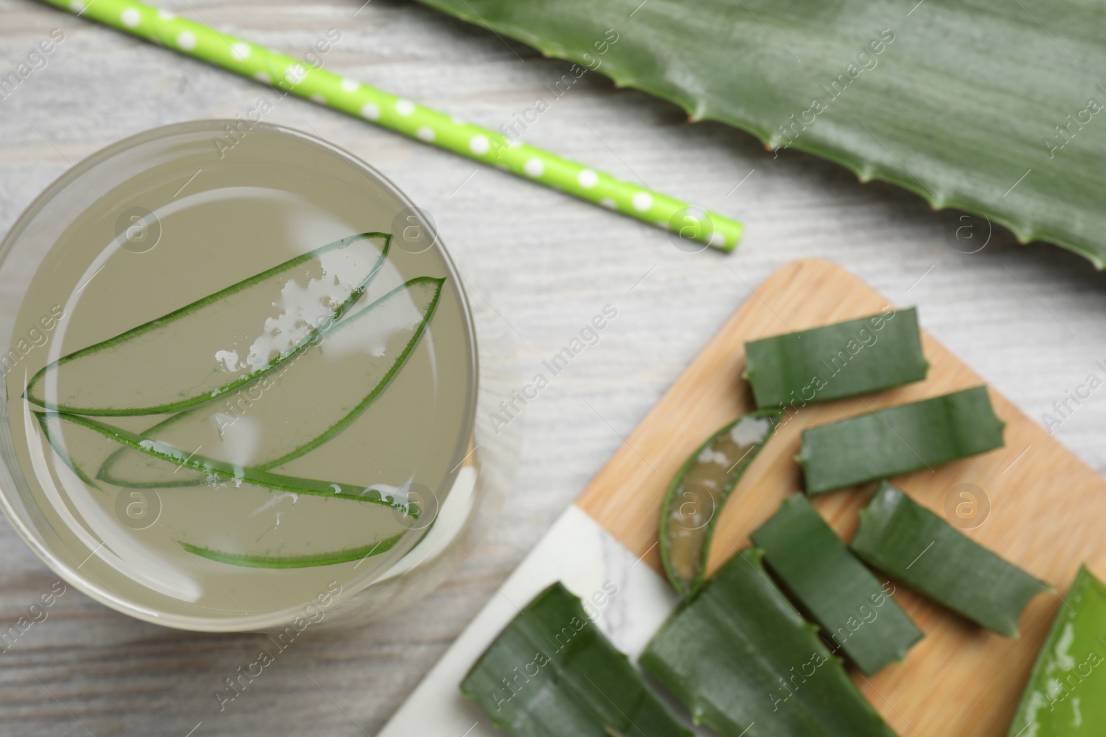 Photo of Tasty aloe juice in glass and fresh leaves on light wooden table, flat lay