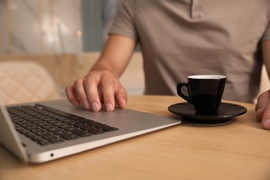 Man with cup of coffee working on laptop at cafe in morning, closeup