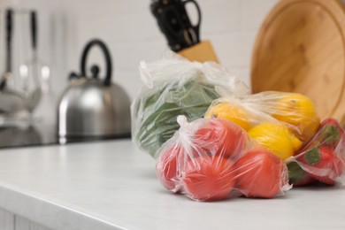 Photo of Plastic bags with different fresh products on white countertop in kitchen. Space for text