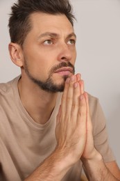 Photo of Man with clasped hands praying on light grey background, closeup