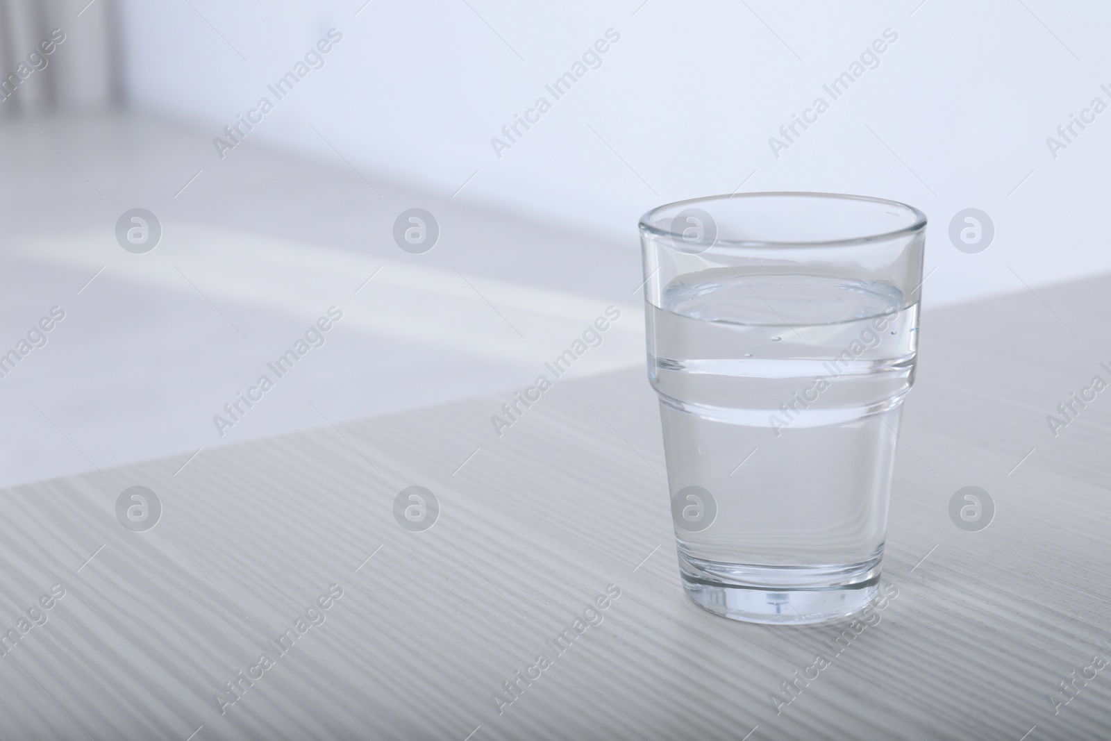 Photo of Glass of water on table against blurred background. Space for text